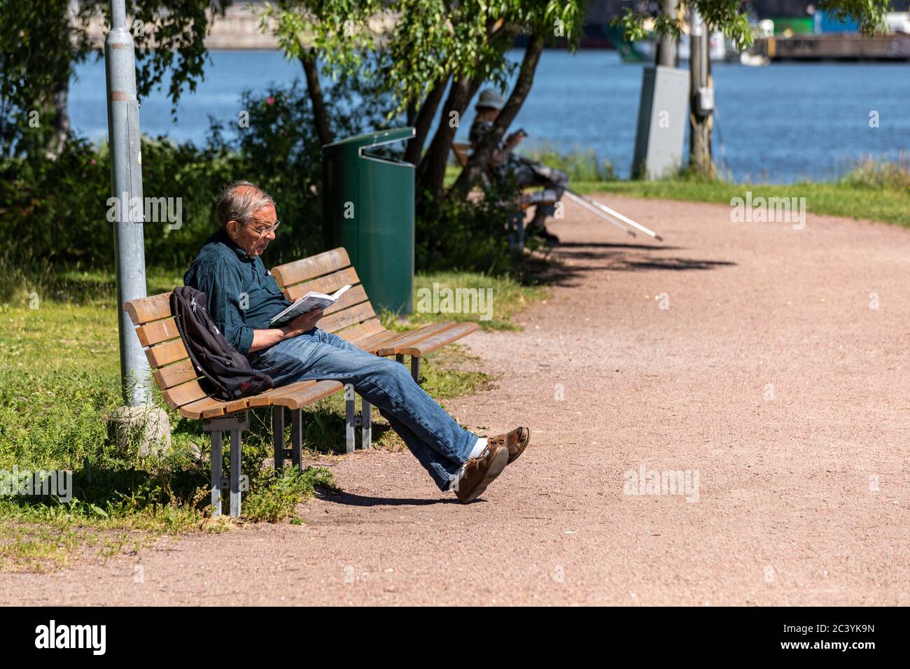Anziano che legge su una panchina dell'isolotto di Tervasaari a Helsinki, Finlandia Foto Stock