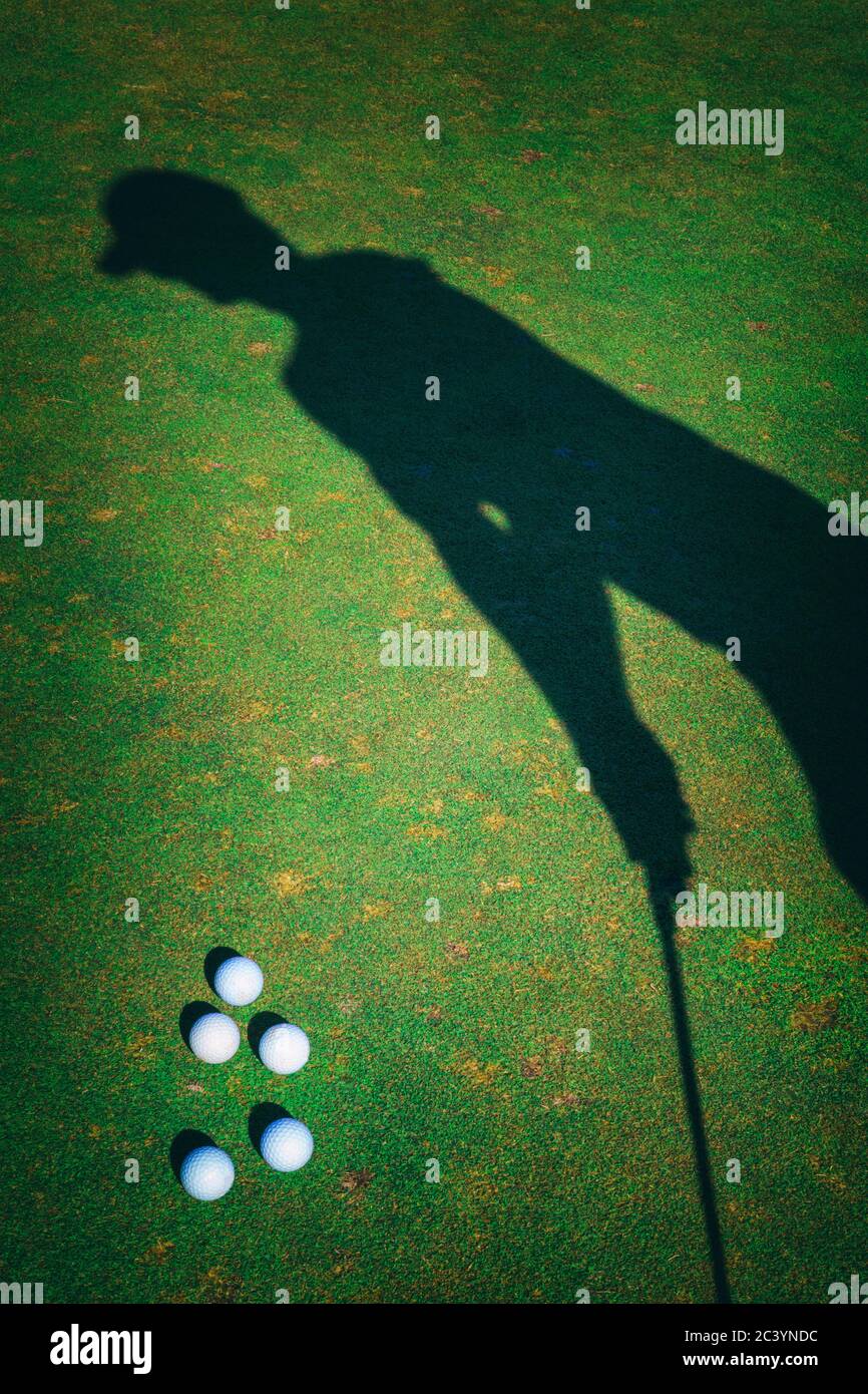 Ombra di golfer che si prepara a colpire la palla sul campo pratica. Palline da golf a terra accanto a lui. Foto Stock