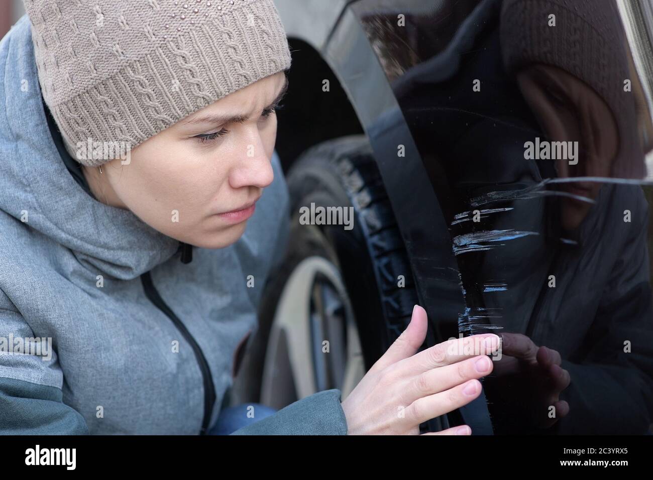 La giovane donna tristemente esamina i graffi freschi sul paraurti di la sua auto Foto Stock