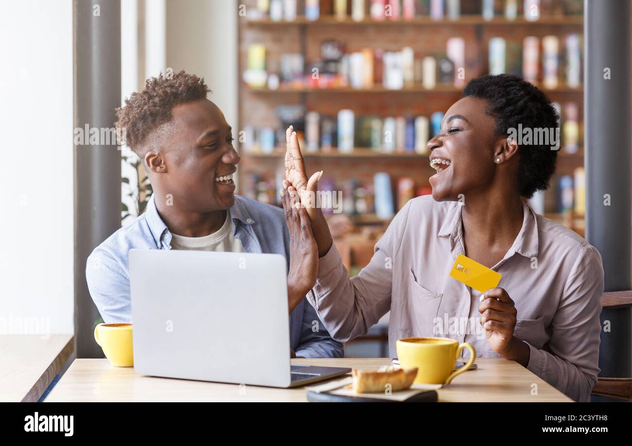 Shopping online. Millennial black coppia con carta di credito che fa cinque gesti alto vicino al portatile al bar Foto Stock