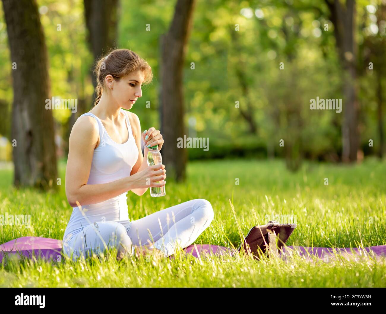 Donna che pratica il fitness e tiene una bottiglia d'acqua sul tappetino yoga Foto Stock