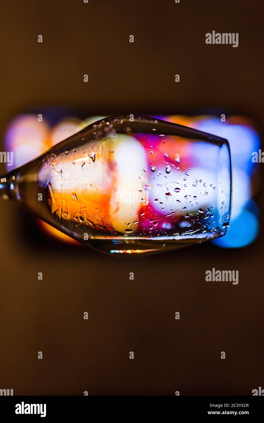 Un primo piano di un bicchiere di vino con gocce di vino bianco, bokeh si illumina sullo sfondo Foto Stock
