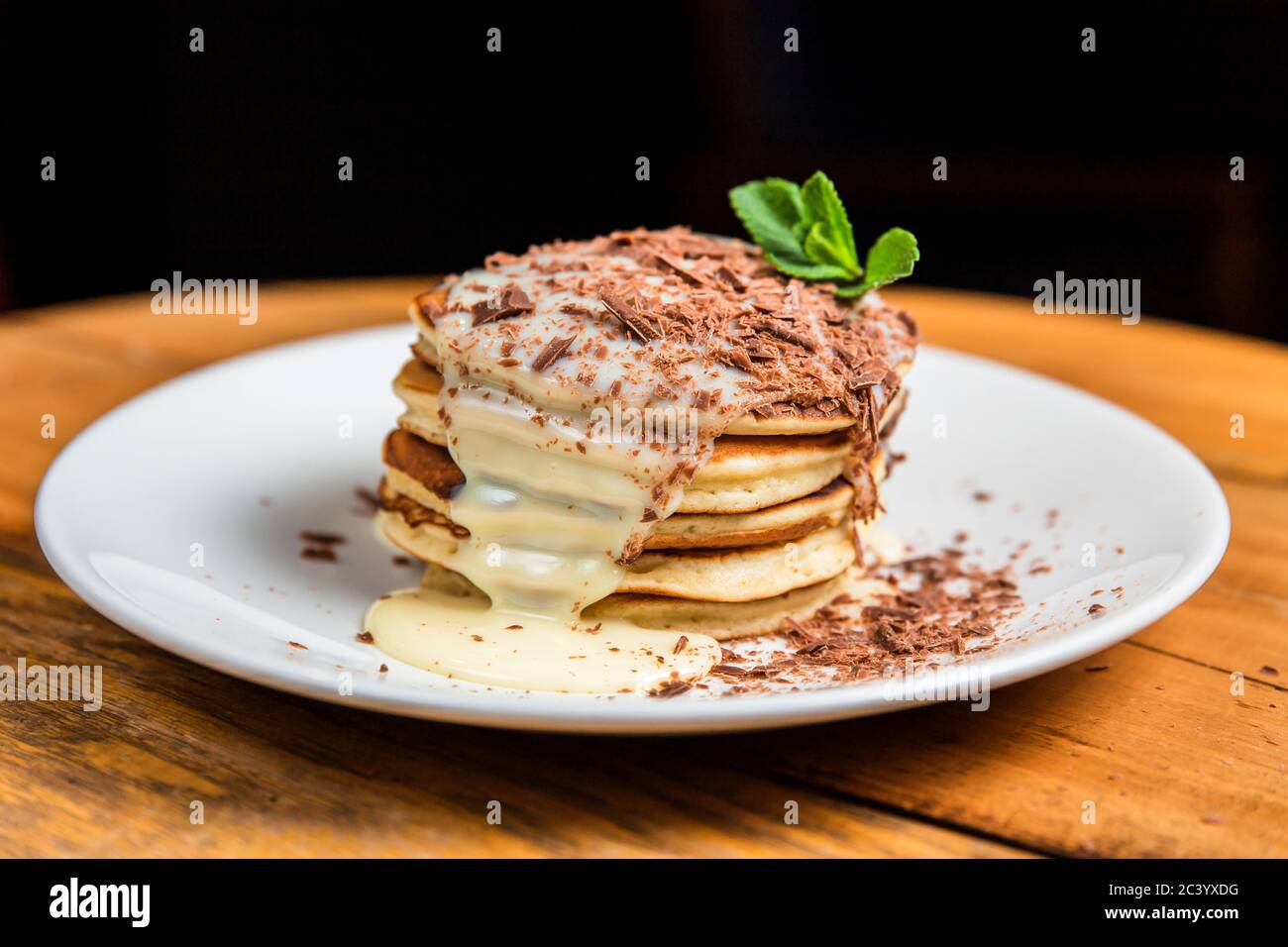 Una pila di frittelle con latte condensato, crumb di cioccolato e menta su un piatto bianco Foto Stock