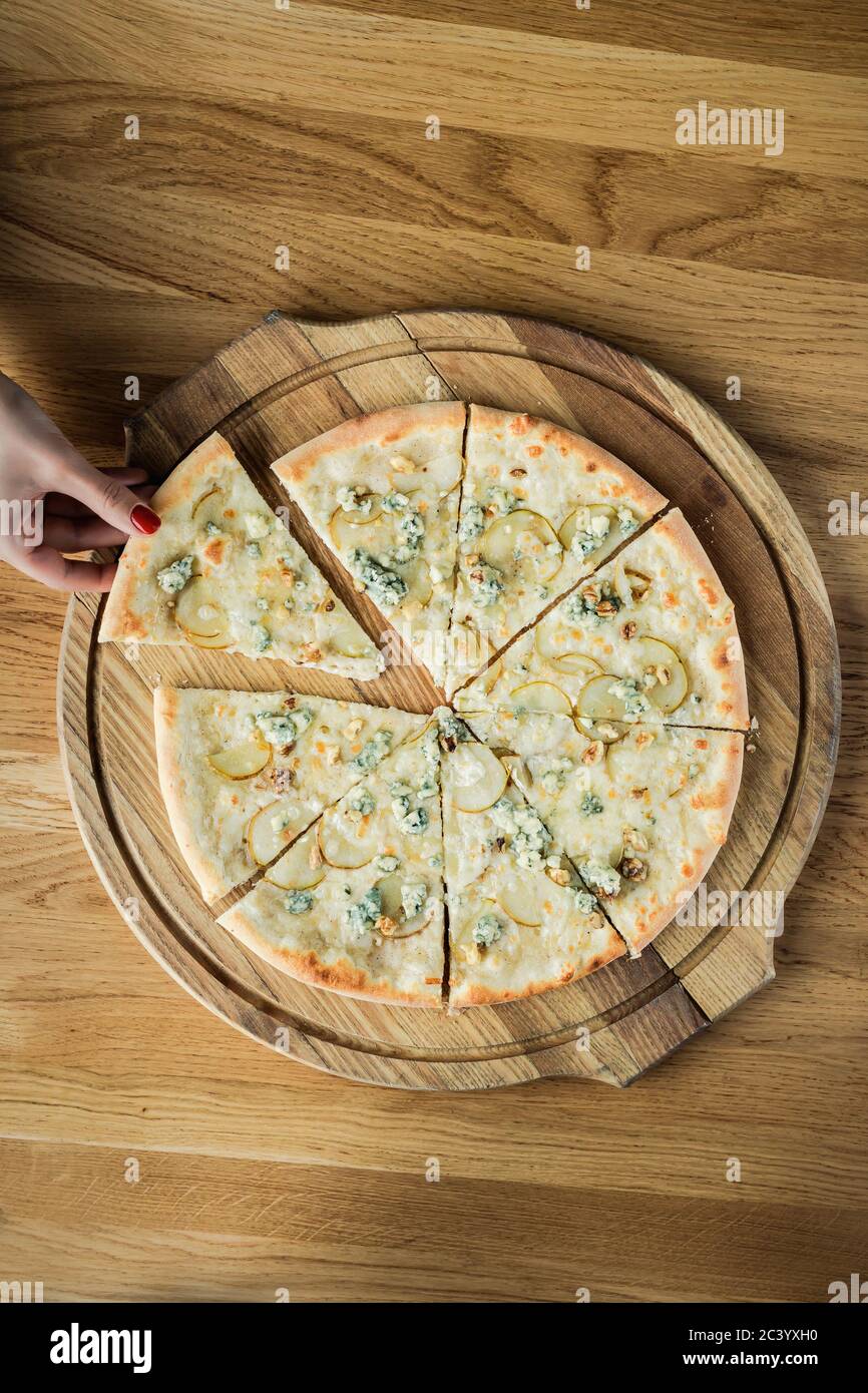 Una mano di donna che rubava una fetta di pizza da una tavola rotonda di legno, foto dall'alto Foto Stock