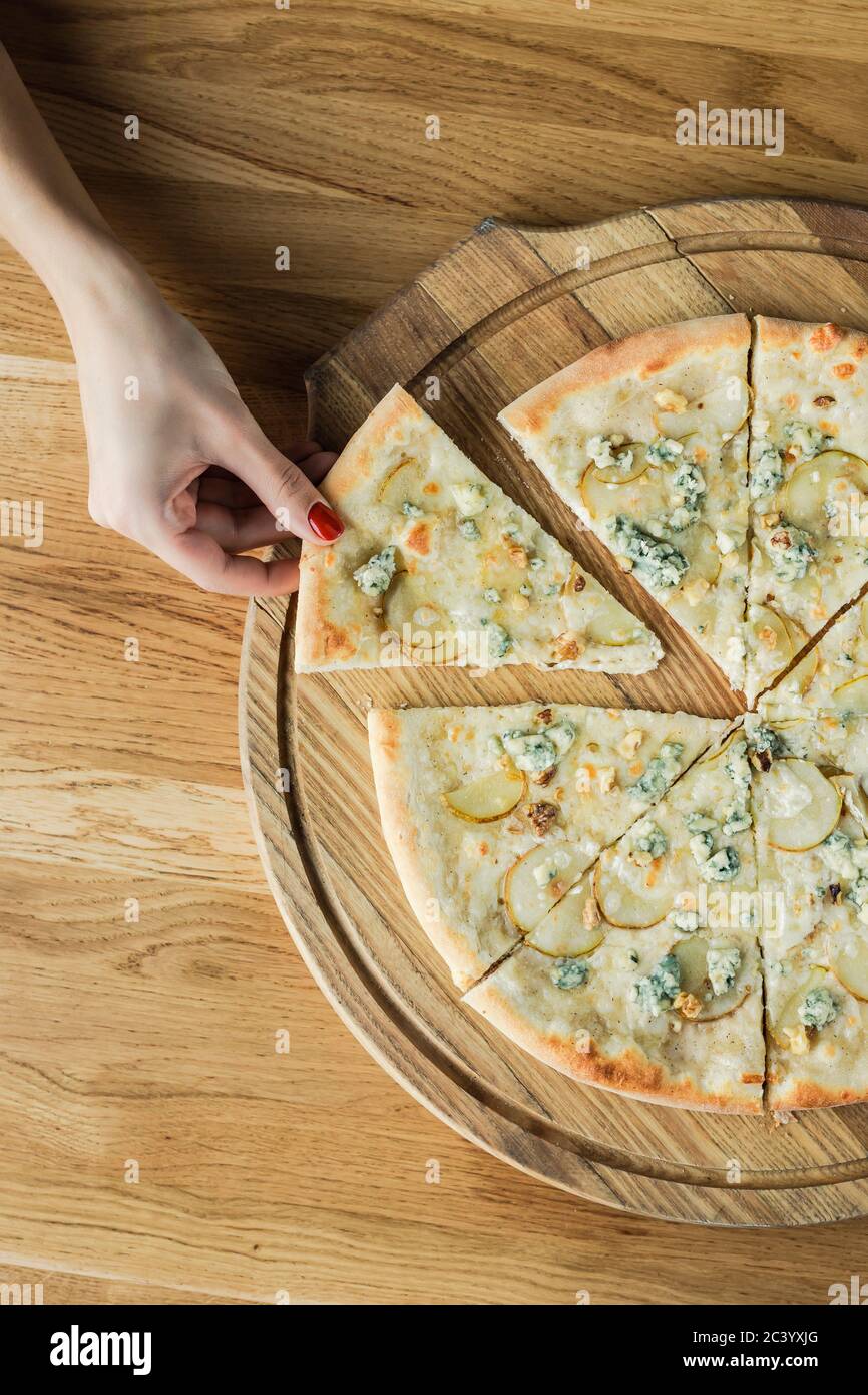 Una mano di donna che rubava una fetta di pizza da una tavola rotonda di legno, foto ravvicinata dall'alto Foto Stock