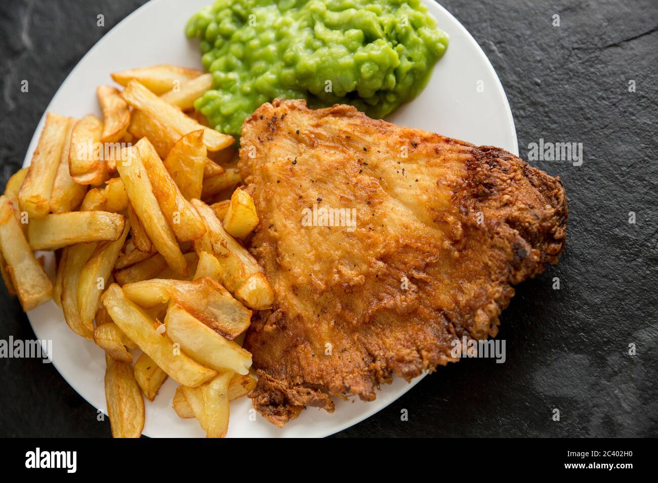Una porzione di pesce e patatine cucinate in casa con piselli. Il pesce è un'ala fritta e martellata da un raggio di spina, Raja clavata, e le patatine sono Foto Stock
