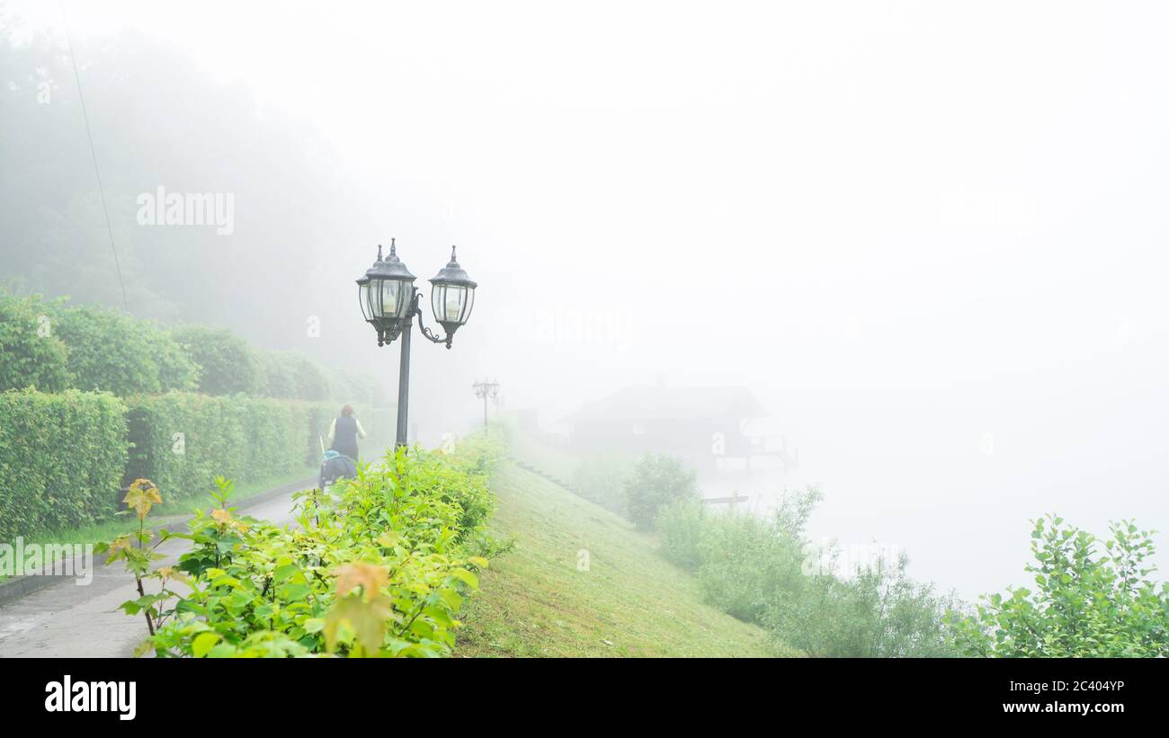 sentiero con lanterne e una verde pendenza al lago con forte nebbia di evaporazione in estate mattina. sfondo Foto Stock