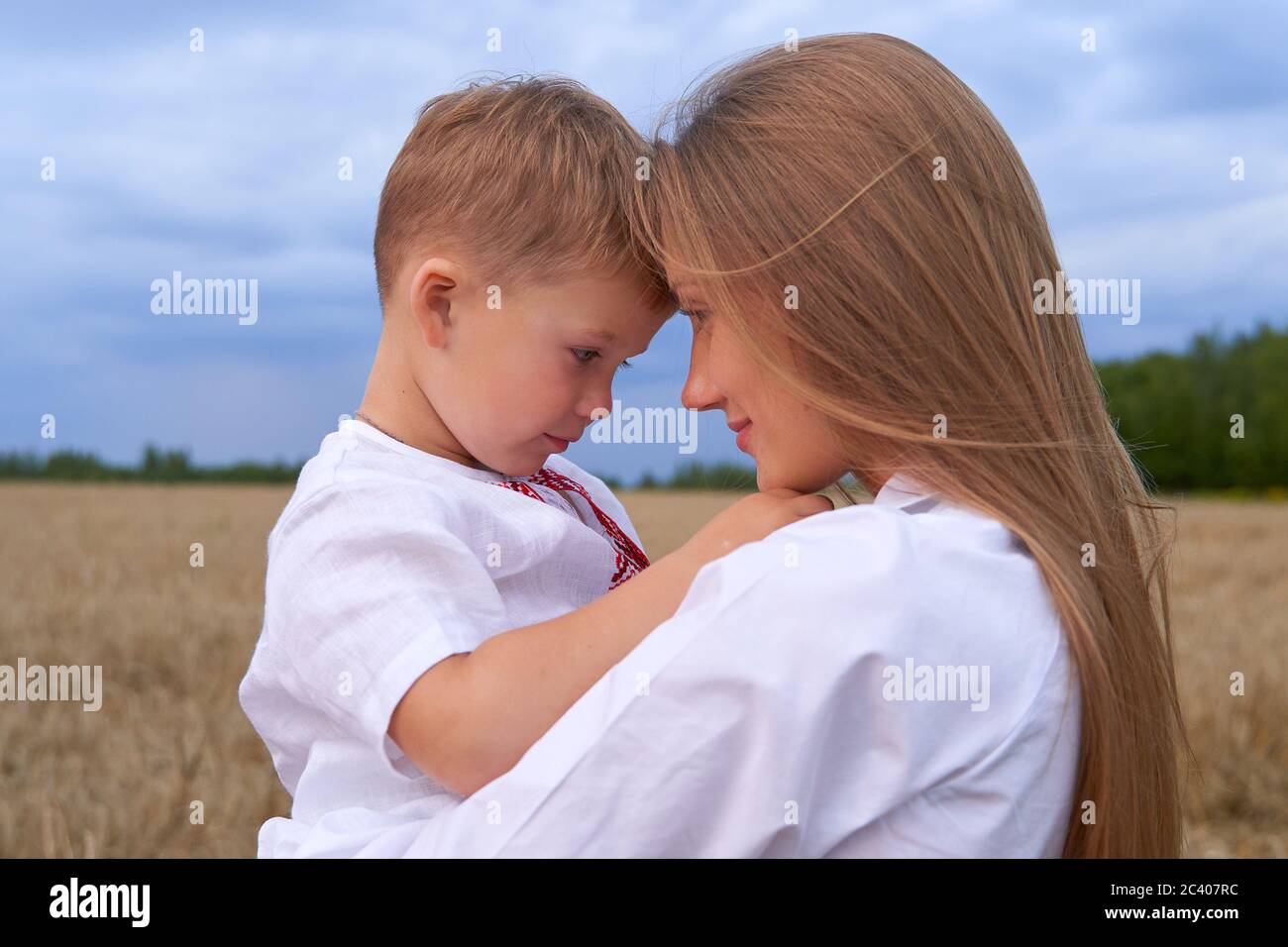 Ritratto di un figlio allegro con una macchina fotografica seduta sulle mamme che si trova in mezzo al campo di grano. Foto Stock