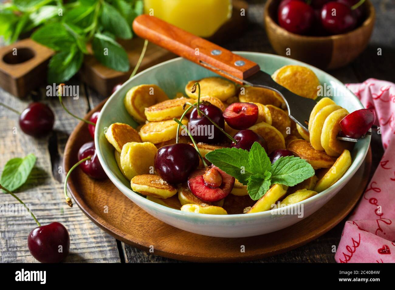Minuscoli pancake, cibo alla moda. Mini pancake con ciliegie e miele su un rustico tavolo in legno. Foto Stock