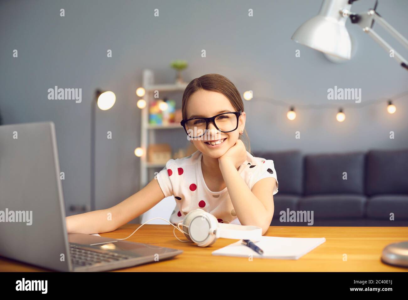 Ritratto di sorridente ragazza di scuola che studia online in soggiorno con computer portatile. Foto Stock