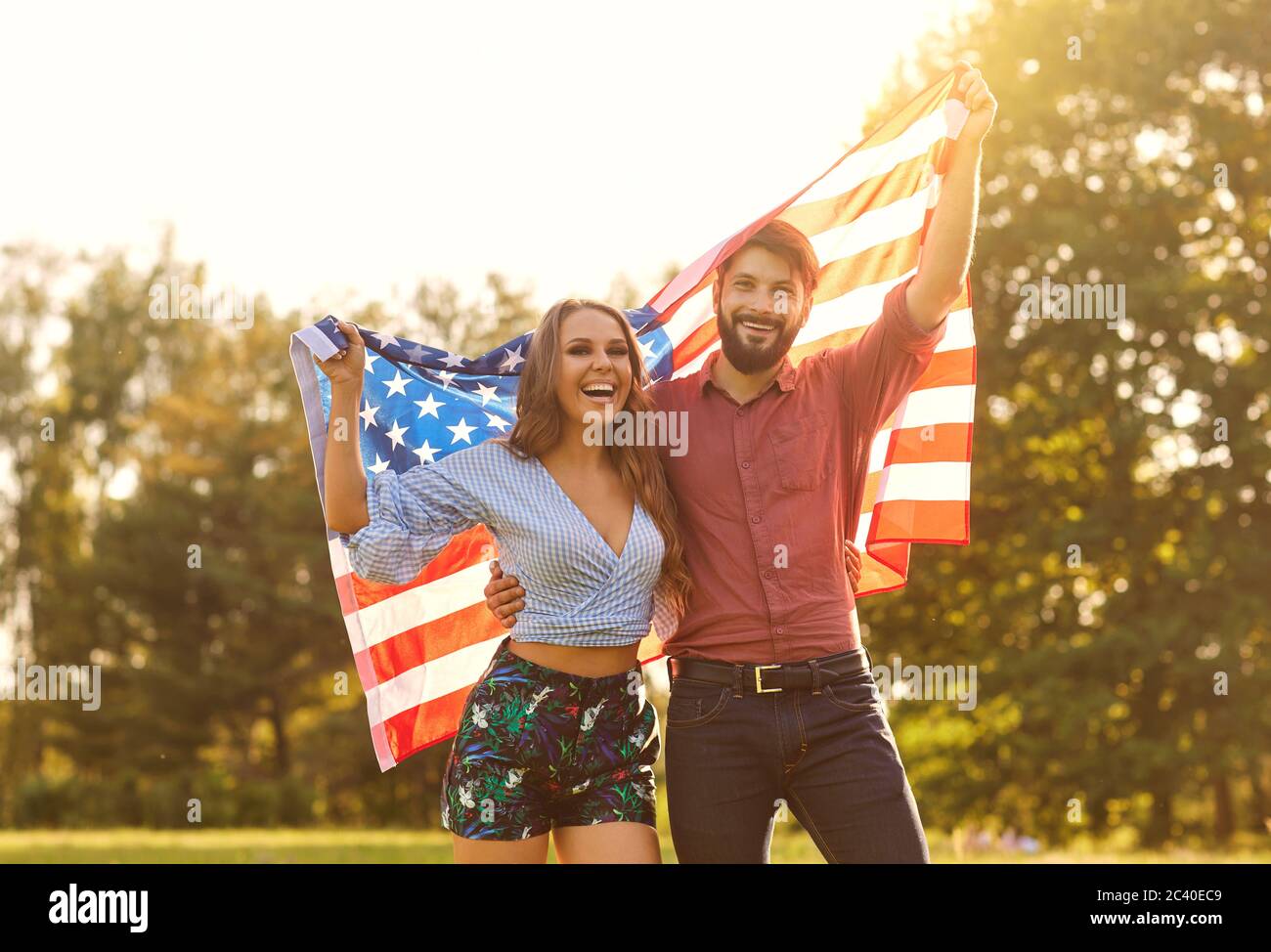 Felice coppia con la bandiera americana che celebra il giorno dell'indipendenza al tramonto. Foto Stock