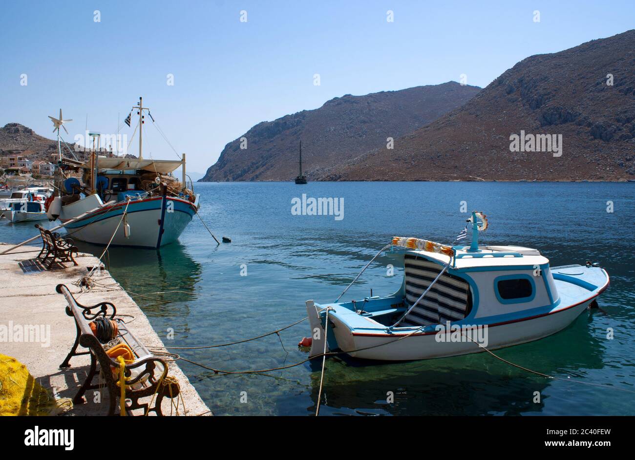 Piccole imbarcazioni da pesca tradizionali ormeggiate nella baia di Pedhi, sulla splendida isola greca di Symi, in una giornata estiva luminosa Foto Stock