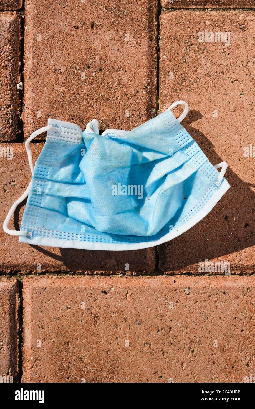 vista ad alto angolo di una maschera chirurgica blu utilizzata gettata sul marciapiede di una strada cittadina Foto Stock