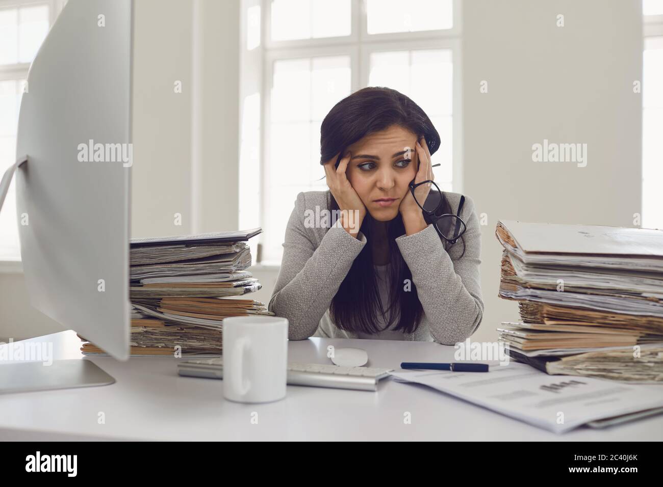 Donna bruna ragioniere in occhiali con una montagna di documenti sul tavolo stanco depresso emaciato depressivo deluso al tavolo nel Foto Stock