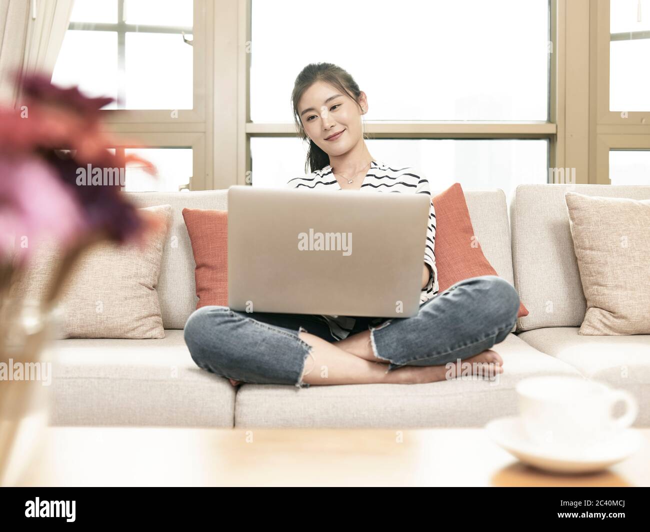 giovane donna d'affari asiatica che lavora da casa seduto sul divano usando un computer portatile Foto Stock