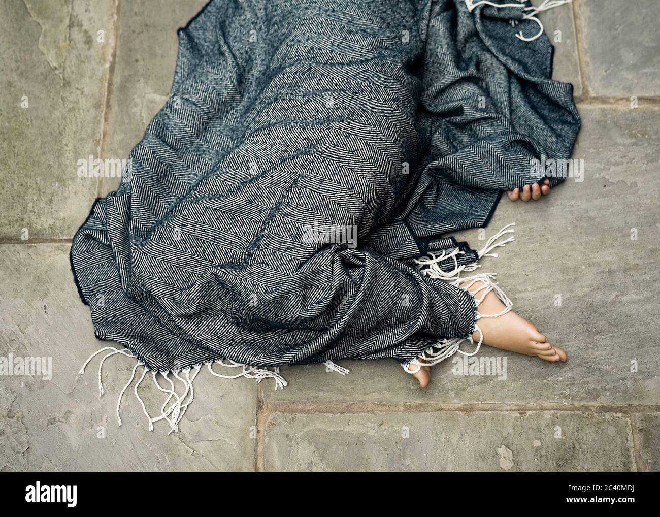 Una figura umana si trova a terra sotto una coperta blu con solo i piedi e alcune dita visibili. Foto Stock