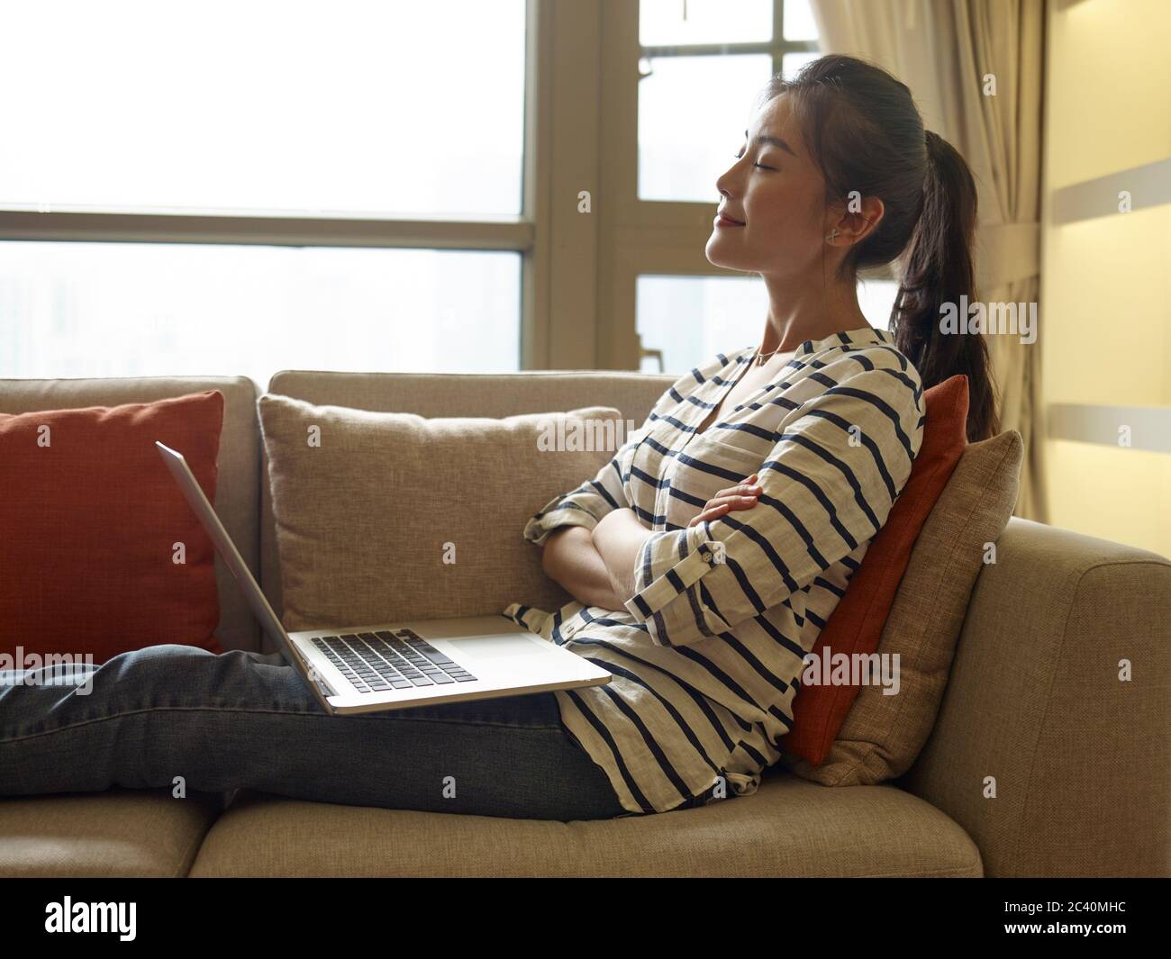 giovane donna asiatica che lavora da casa seduta sul divano usando un computer portatile Foto Stock