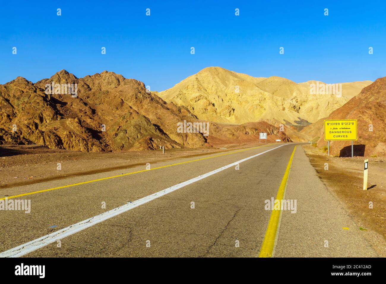 Vista della strada del deserto 12, con un segnale trilingue di avvertimento (curve pericolose) e paesaggio. Montagne di Eilat, Israele meridionale Foto Stock