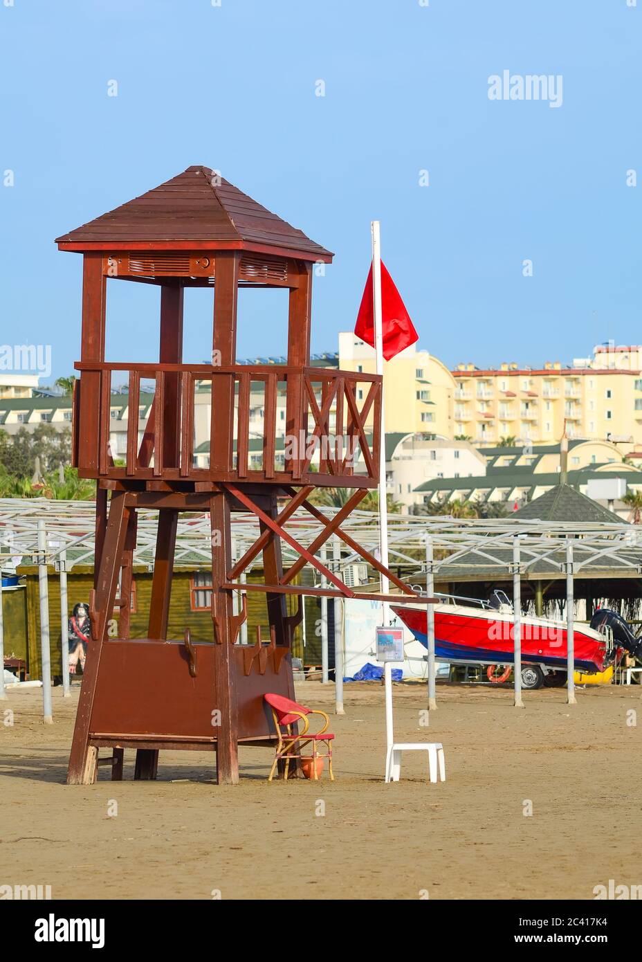 Torre di bagnino su una spiaggia vuota con una bandiera rossa sollevata. Un cartello che proibisce di nuotare in mare. Foto Stock