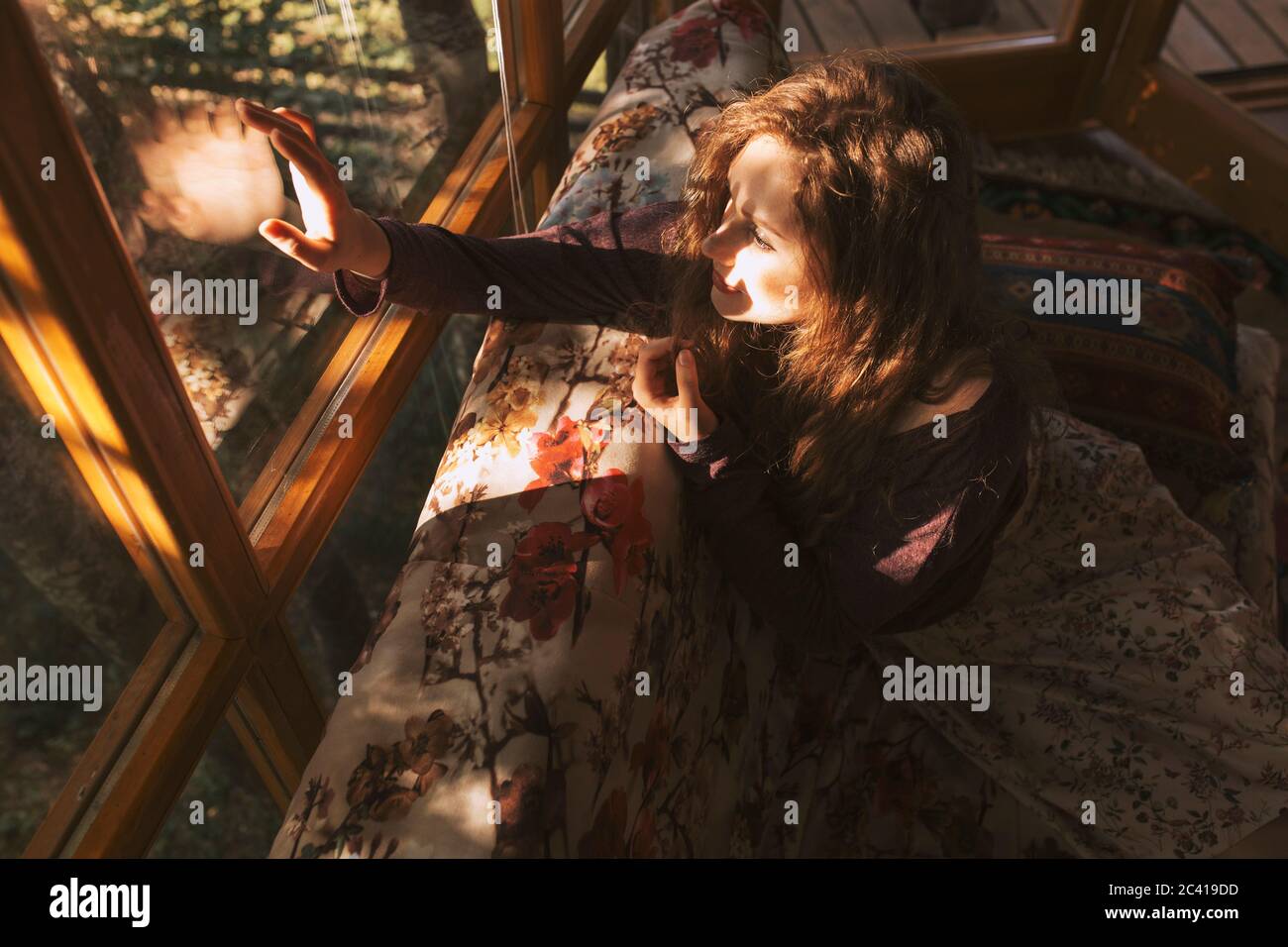 Giovane donna rossa seduta sul divano e guardando attraverso la finestra Foto Stock