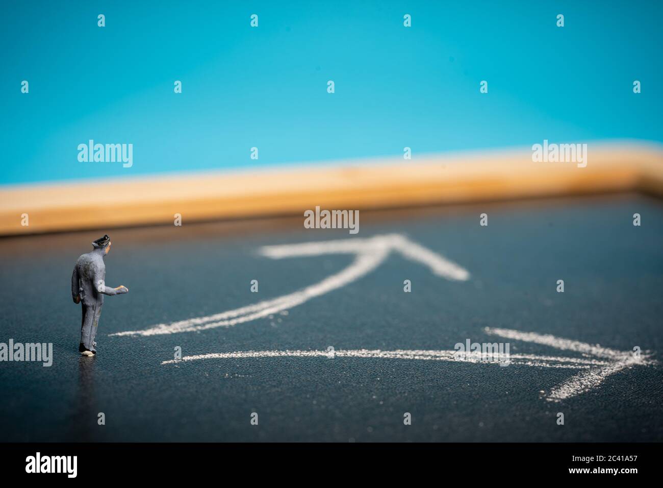 Concetto di business: Processo decisionale. Uomo in miniatura sulla lavagna con due frecce che puntano in direzioni diverse Foto Stock
