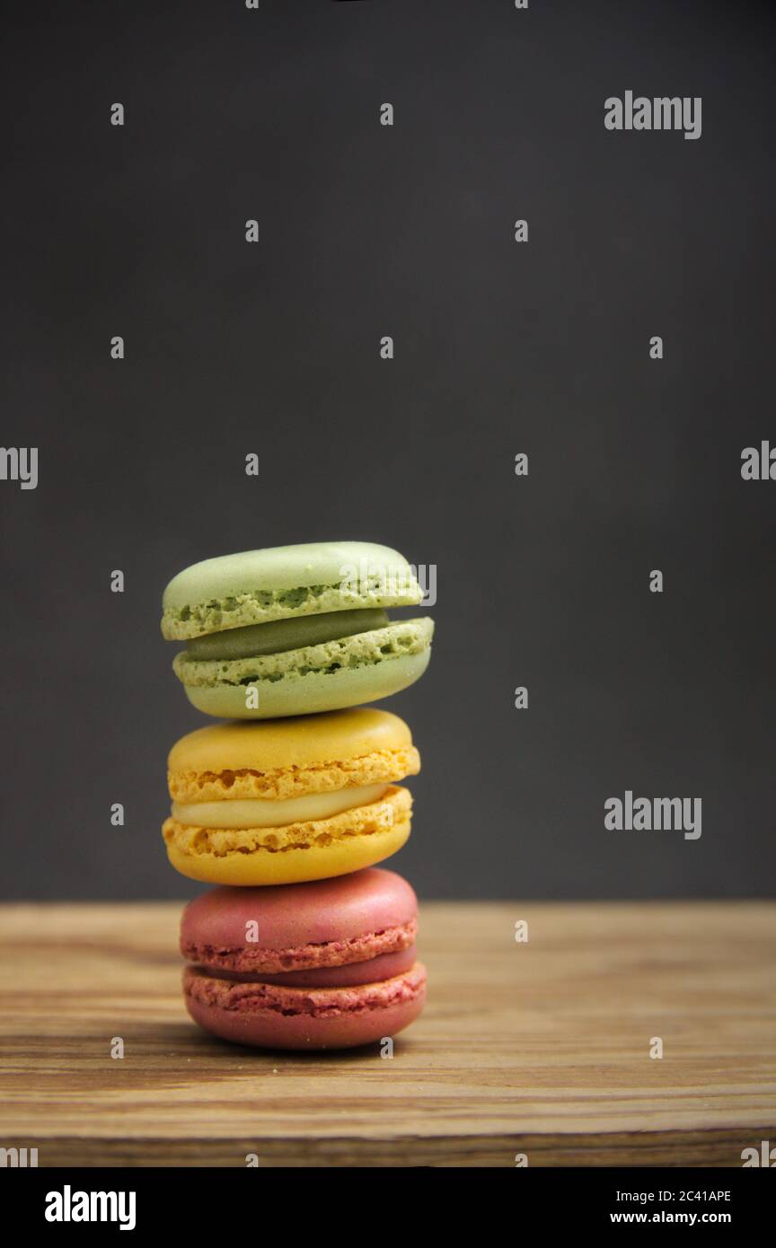 Una pila di macaron di sapori e colori diversi su un tavolo di legno con sfondo scuro, luce laterale e spazio di copia Foto Stock