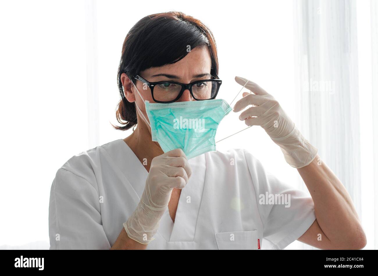 Infermiere con occhiali e guanti in lattice che si indossa su una maschera chirurgica Foto Stock