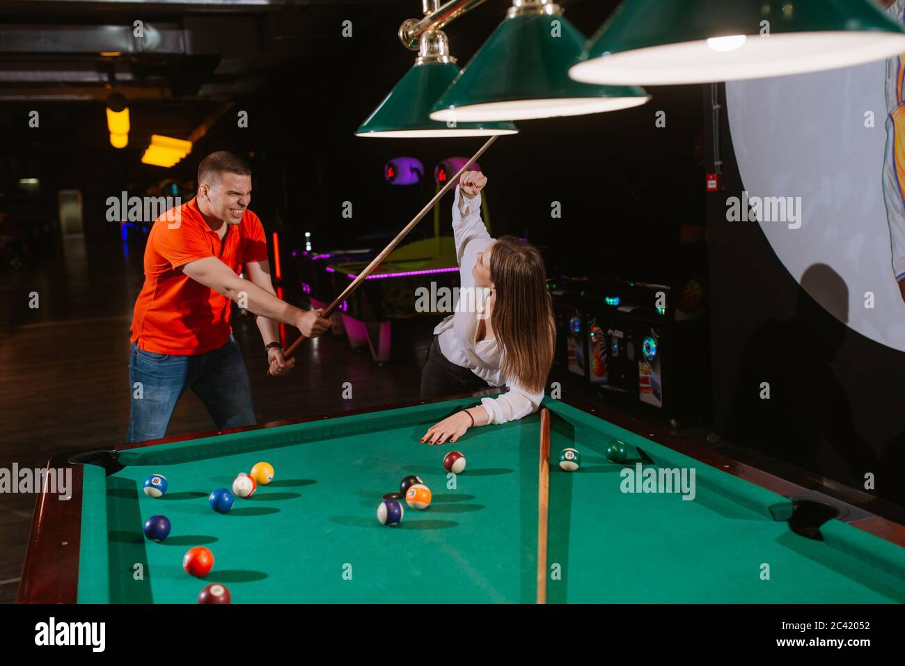 Una bella giovane donna caucasica e un uomo caucasico si colpiscono a vicenda con spunti da biliardo. Amore e divertimento Foto Stock