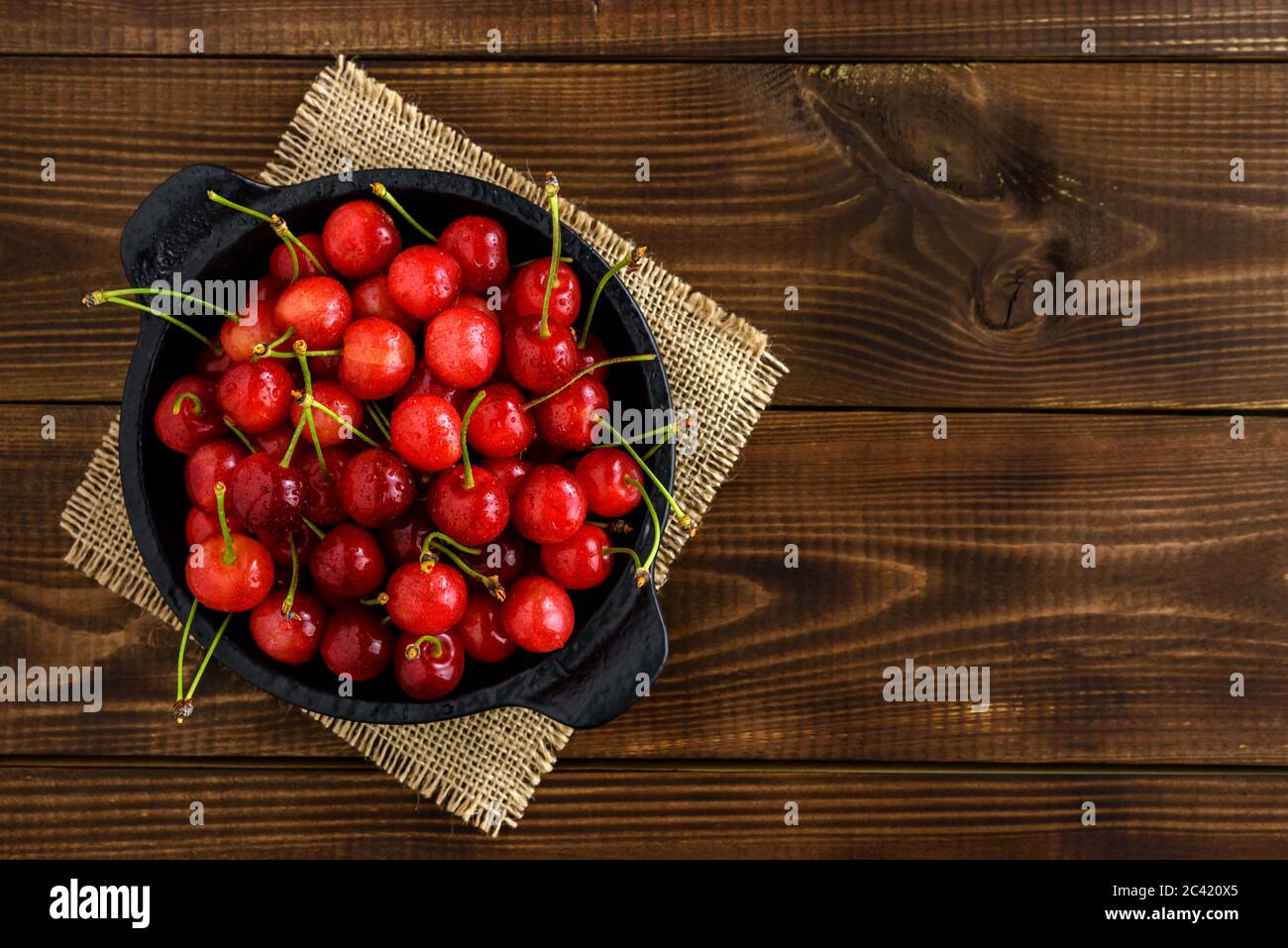Ciliegie rosse dolci in una ciotola nera su un tavolo di legno marrone scuro con spazio per la copia del testo. Vista dall'alto. Foto Stock