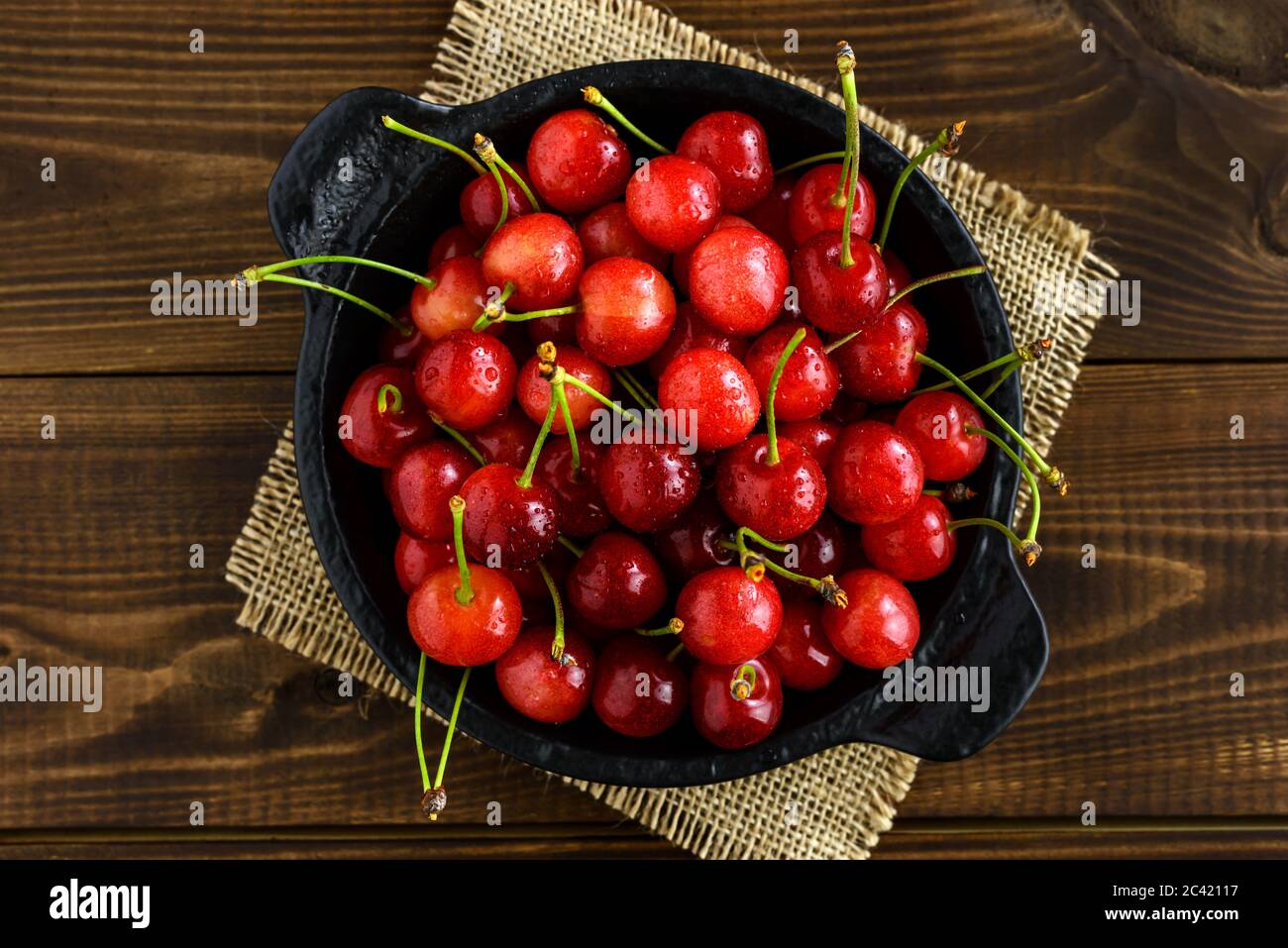 Ciliegie rosse dolci in una ciotola nera su un tavolo di legno marrone scuro. Vista dall'alto. Foto Stock