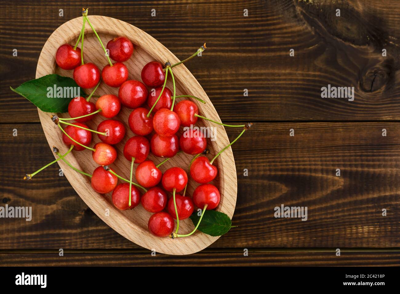 Ciliegie rosse dolci in una ciotola ovale di legno su un tavolo di legno con spazio per la copia del testo. Vista dall'alto. Foto Stock