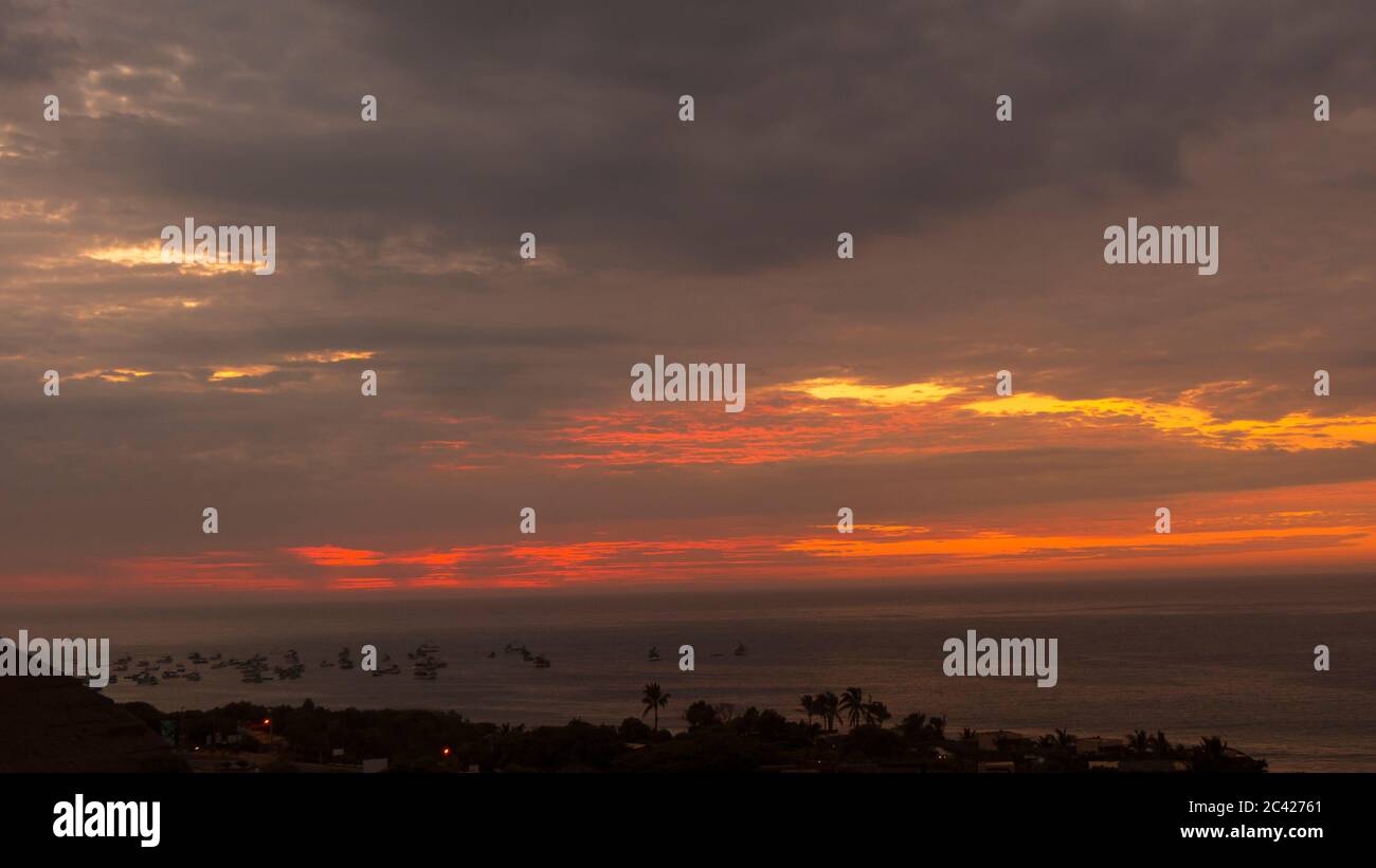 Vista di un tramonto nuvoloso sulla costa con gruppo di barche in mare Foto Stock