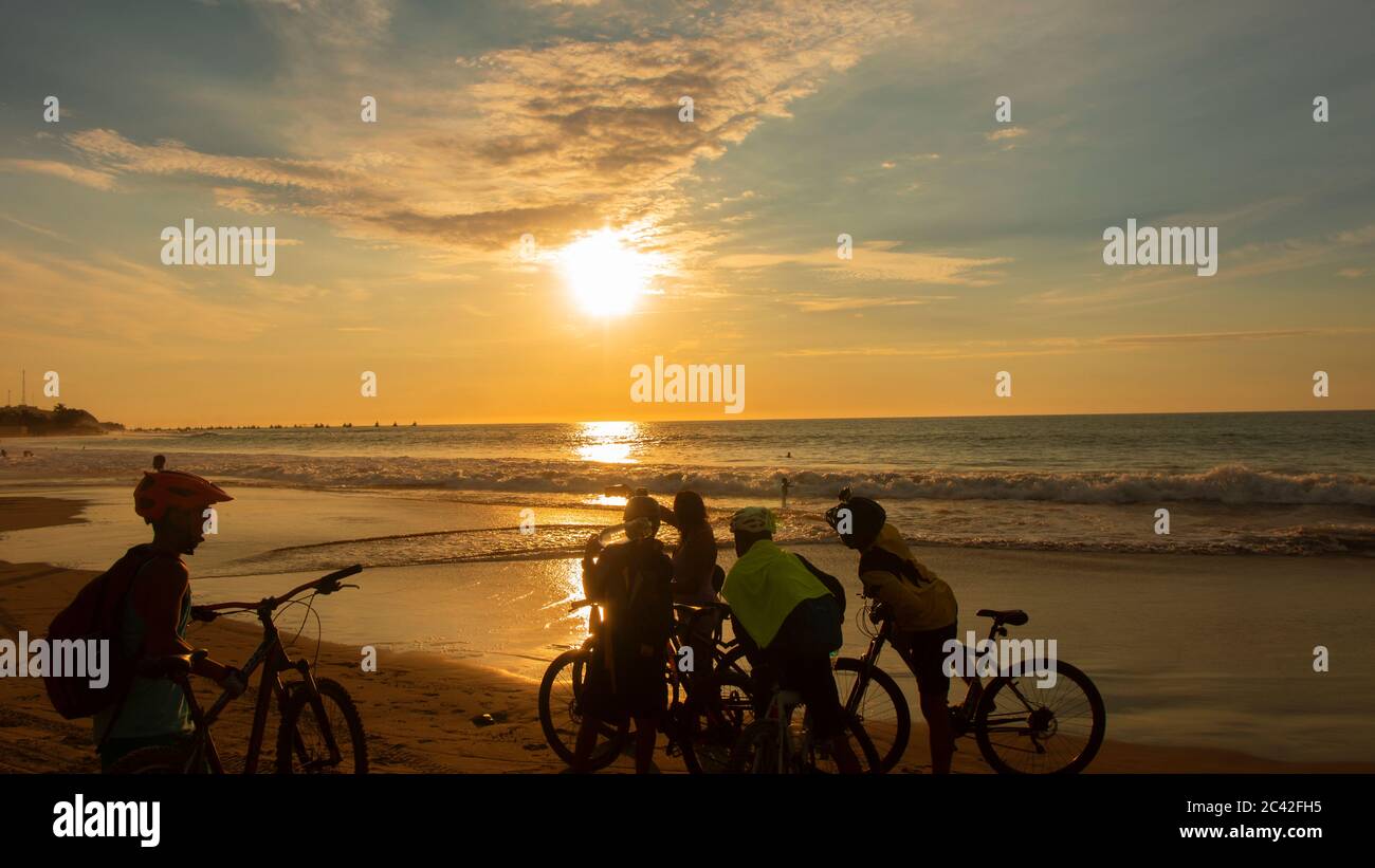 Mancora, Piura / Perù - 7 aprile 2019: Gruppo di ciclisti che scatta una foto sulla spiaggia durante il tramonto con il sole che si riflette sul mare Foto Stock