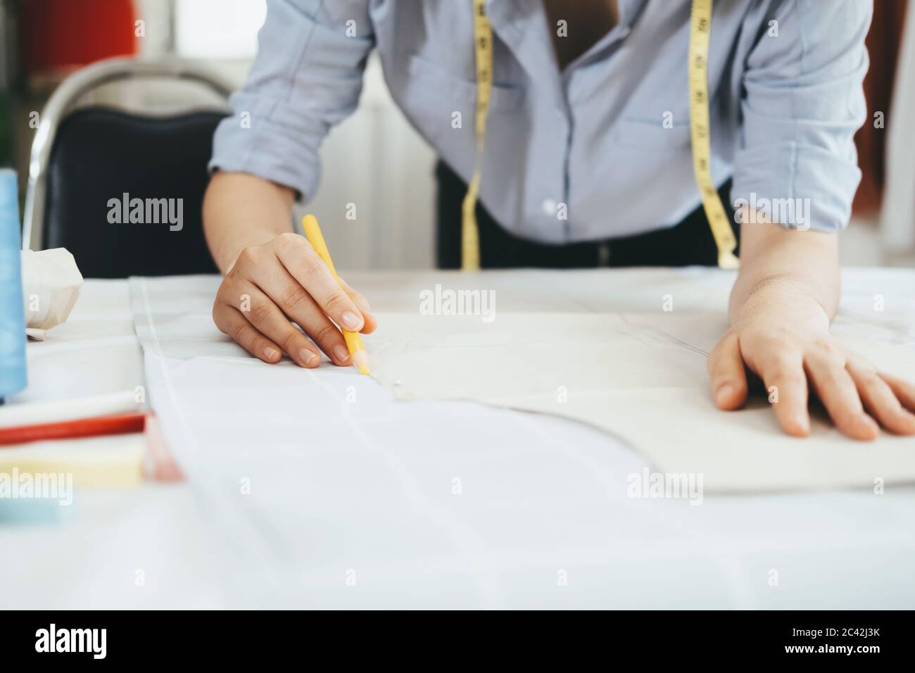 Primo piano giovane sarto lavorazione con disegno di cucitura linea su tessuto con gesso a matita. Foto Stock