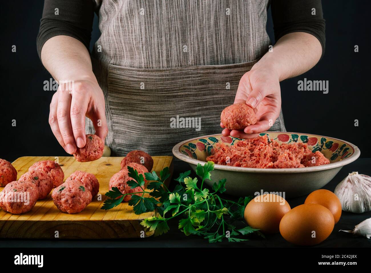 La cuoca forma la carne macinata per preparare polpette fatte in casa condendole con spezie diverse per il sapore. Foto Stock