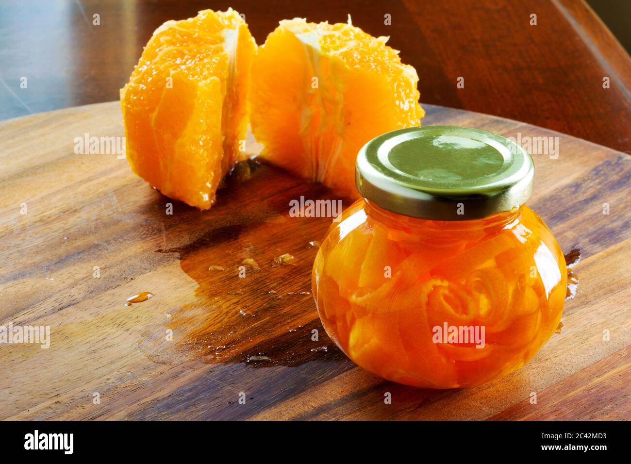 Un piccolo vasetto di marmellata fatto da bucce d'arancia è seduto su un tagliere di legno. Due metà di un arancio pelato sono sul retro. Foto Stock