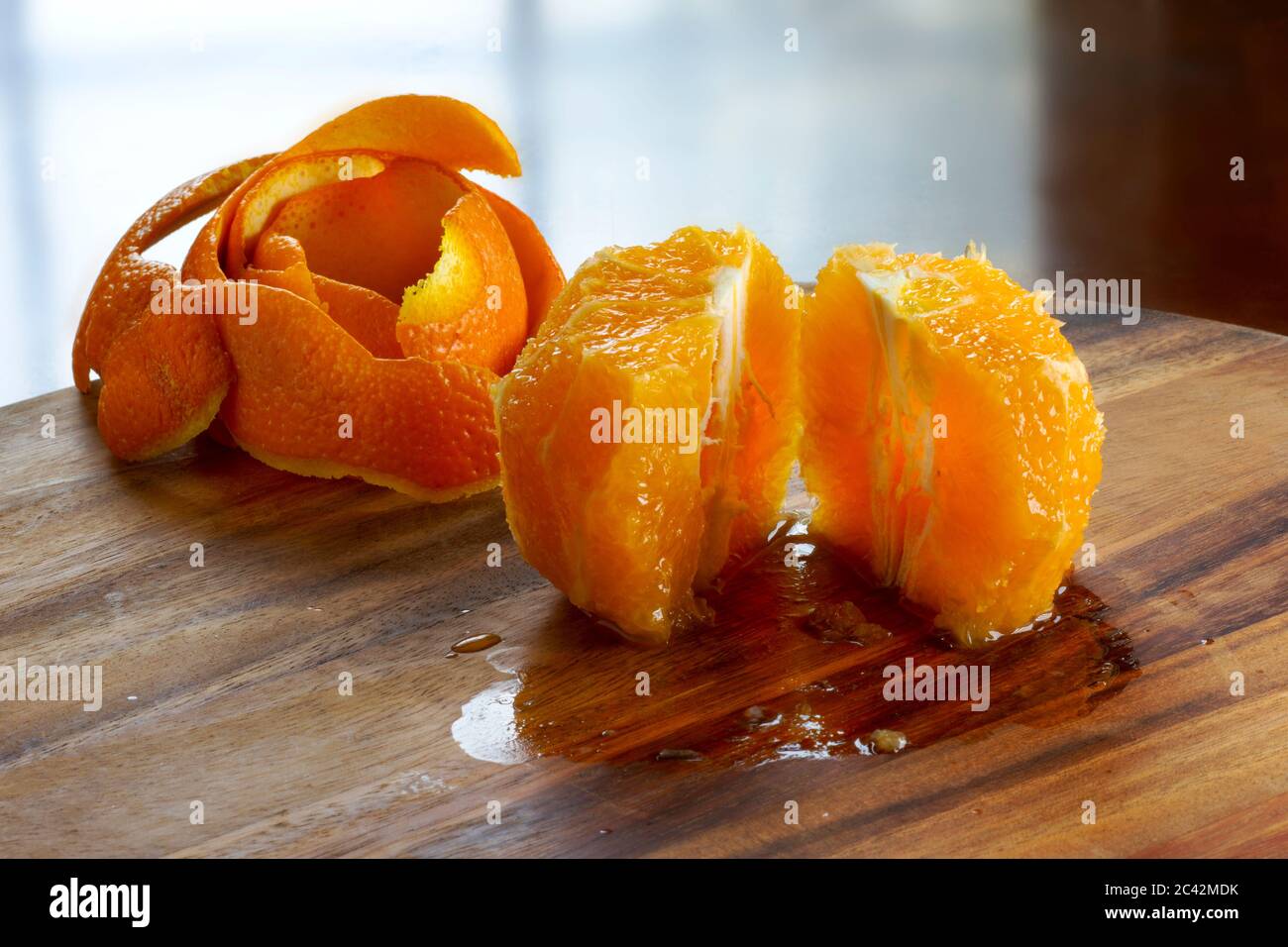 Un arancio pelato a metà posto su un tagliere di legno, retroilluminato con una luce della finestra. Il tavolo è bagnato dal succo d'arancia. Buccia d'arancia sul retro. Foto Stock