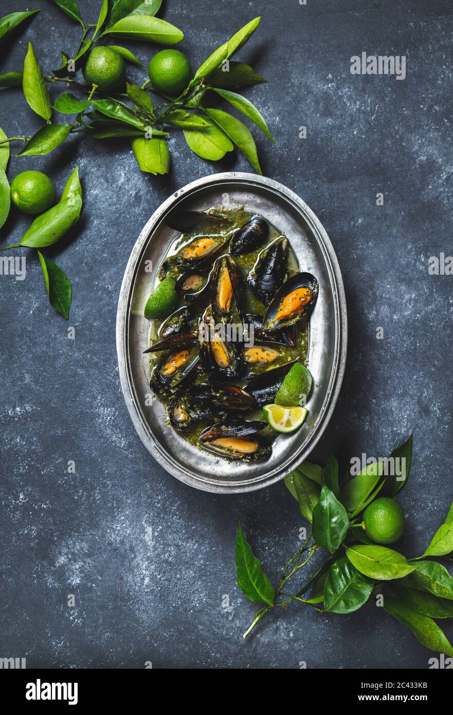 Cozze in erba verde e salsa di vino bianco con limone su fondo scuro. Foto Stock