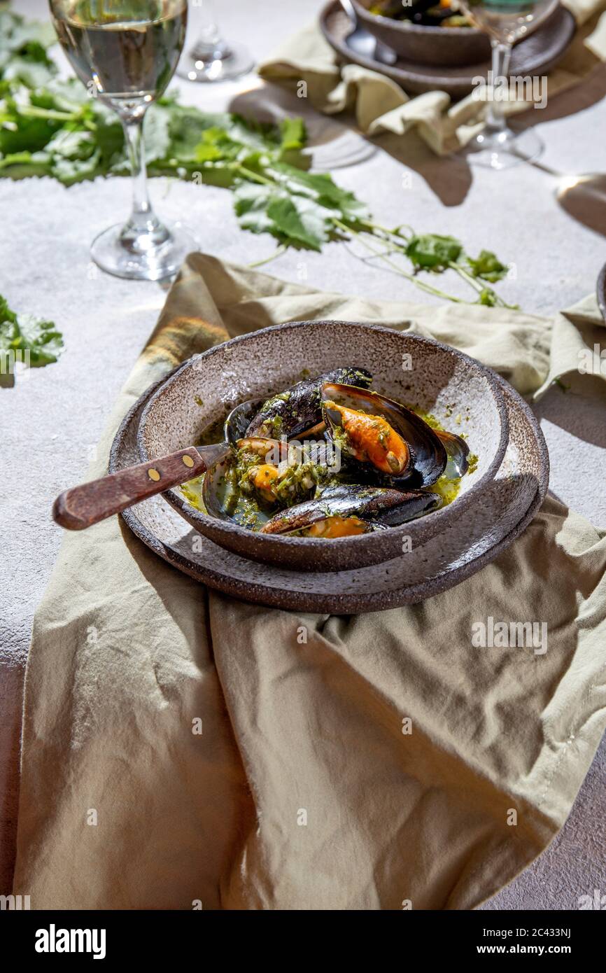 Cena in stile mediterraneo. Primo piano di tavola con cozze in salsa verde e vino bianco. Foto Stock