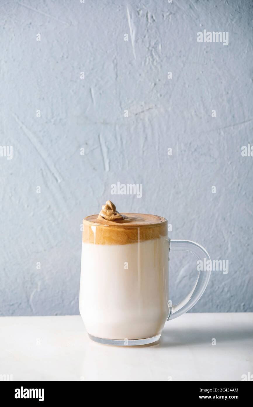 Dalgona Frothy caffè tendenza bevanda coreana latte latte latte con schiuma di caffè in tazza di vetro su tavolo di marmo bianco. Spazio di copia Foto Stock