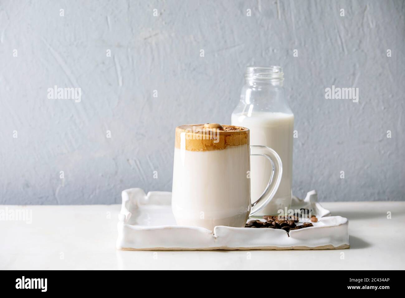 Dalgona Frothy Coffee trend bevanda coreana latte latte latte con schiuma di caffè in tazza di vetro su vassoio in ceramica con ingredienti su tavolo di marmo bianco. Foto Stock
