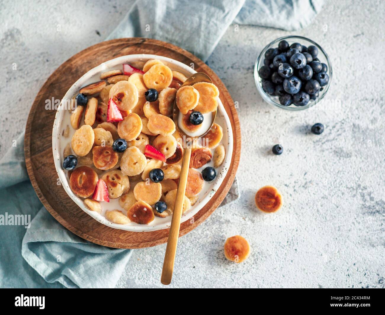 Cibo alla moda - cereali pancake. Latte con pancake carei nel recipiente. Minuscoli pancake di cereali con bacche in piatto artigianale su fondo grigio di cemento. Copia sp Foto Stock