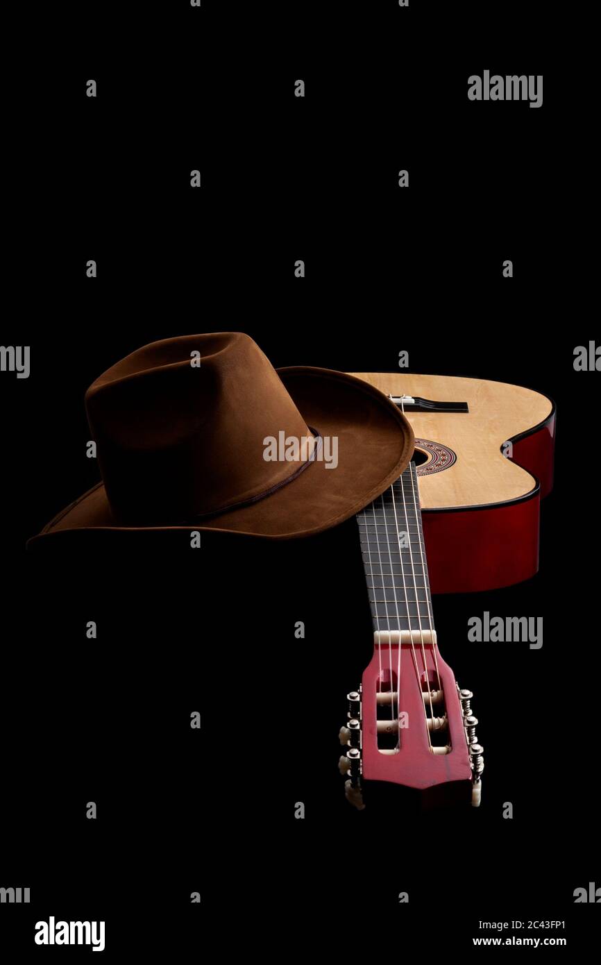 Cultura americana, canzone popolare e tema di concetto muisc paese con un cappello cowboy e una chitarra acustica isolato su sfondo nero con luci drammatiche Foto Stock