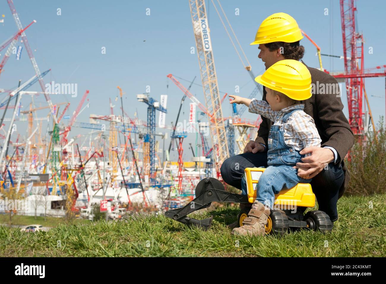 Padre e figlio con caschi da costruzione davanti alle gru da costruzione Foto Stock