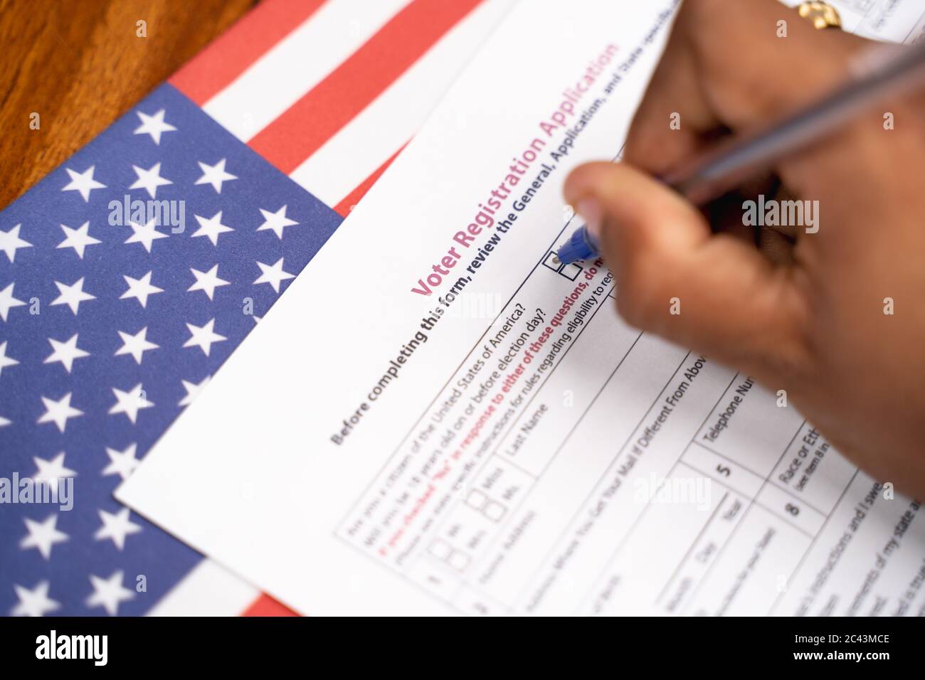 Maski, India - 23, Giugno 2020 : primo piano di mani che riempiono la domanda di registrazione del presidente voter con la bandiera degli Stati Uniti come sfondo per le prossime elezioni. Foto Stock
