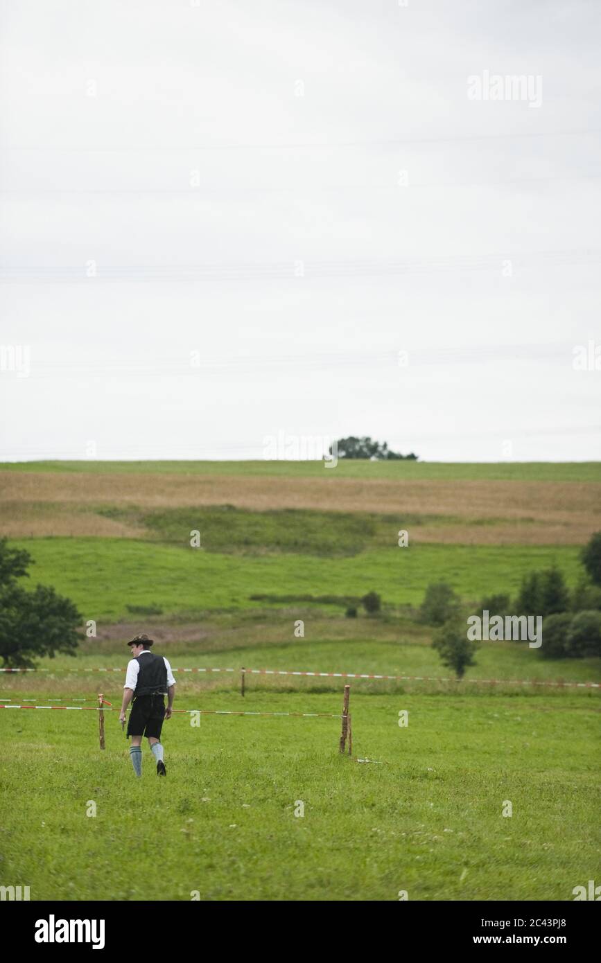 Uomo in abiti tradizionali bavaresi cammina attraverso un campo Foto Stock