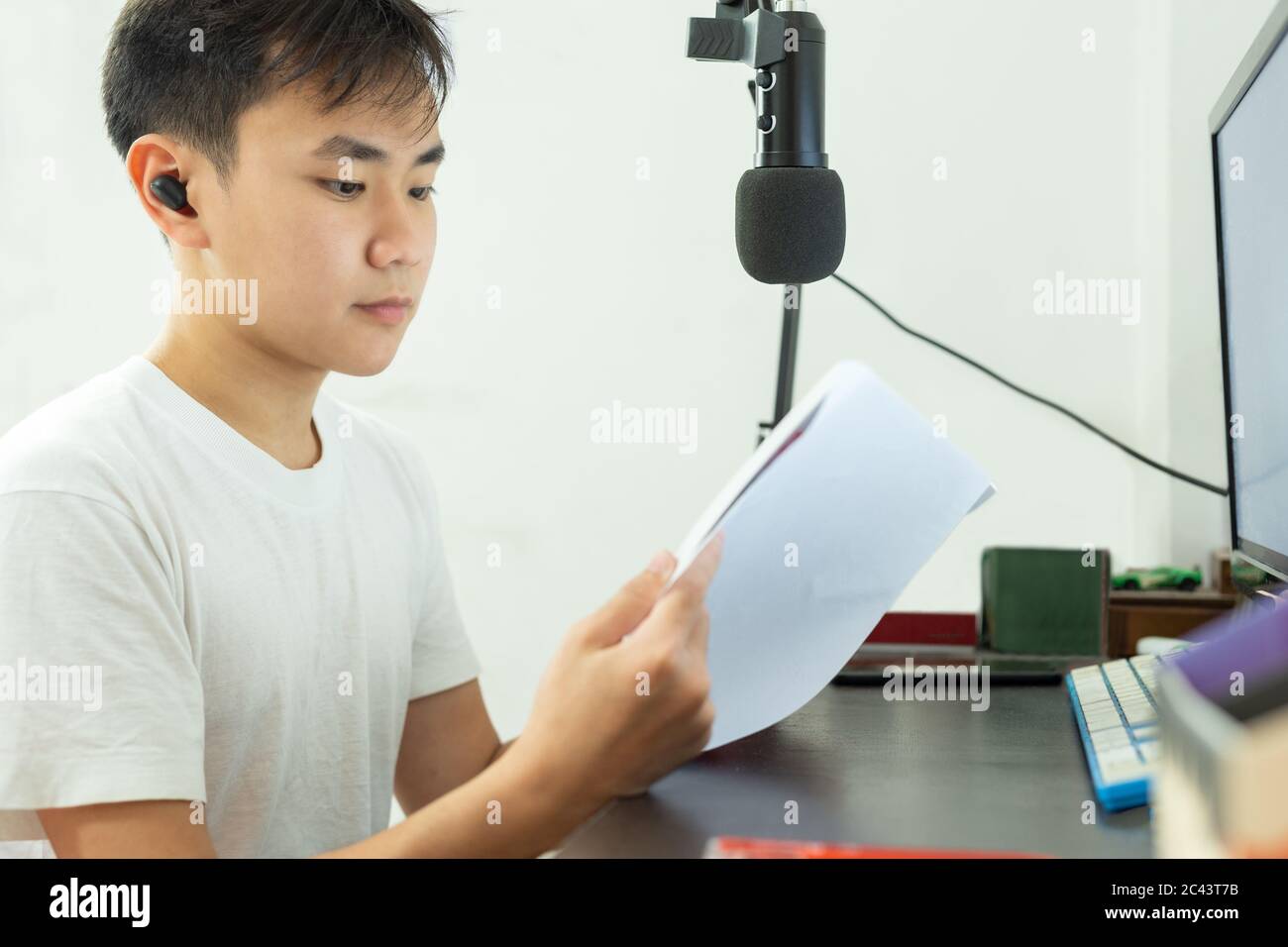 Un ragazzo asiatico studia su un libro con microfono e pc sul tavolo di studio a casa. Foto Stock