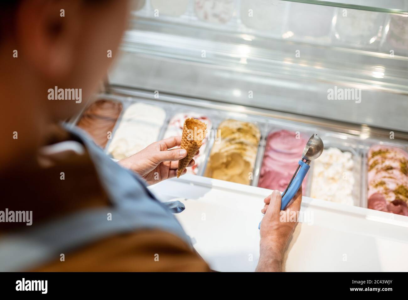 Venditore che raccoglie il gelato con un cucchiaio dal frigorifero nel negozio. Vista dall'alto su un vassoio pieno di gelato con sapori diversi Foto Stock
