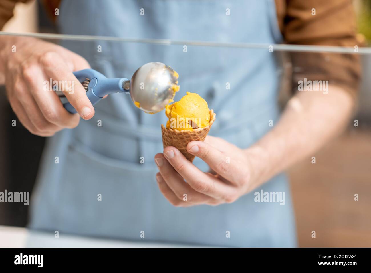 Venditore che mette le palle del gelato nel cono del waffle, vendendo i dolci al negozio, primo piano Foto Stock