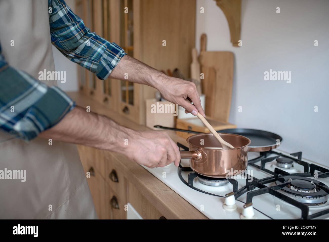 Uomo in una camicia a scacchi e grembiule mettendo la padella sul forno Foto Stock